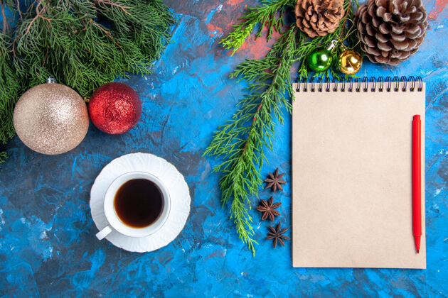 圣诞顶视图红色铅笔放在笔记本上松树枝圣诞装饰一杯茶放在蓝色的表面颜色杯子视图