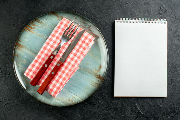 餐巾顶视图刀叉放在红白方格餐巾上放在圆板笔记本上放在黑桌子上粉末方格笔记本
