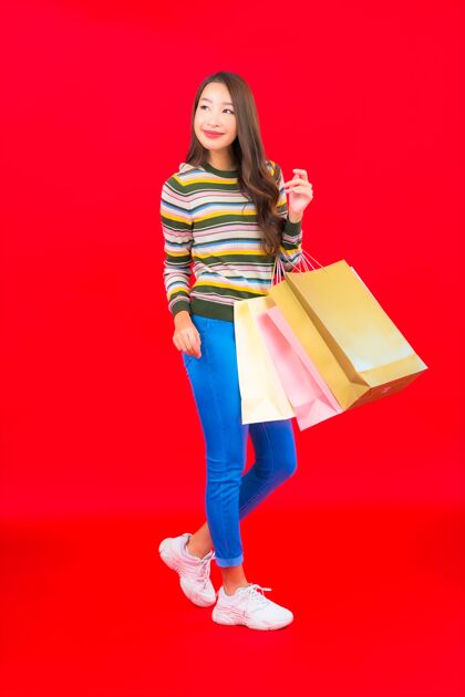 亚洲在红墙上画一幅美丽的亚洲年轻女子 带着五颜六色的购物袋快乐折扣银行