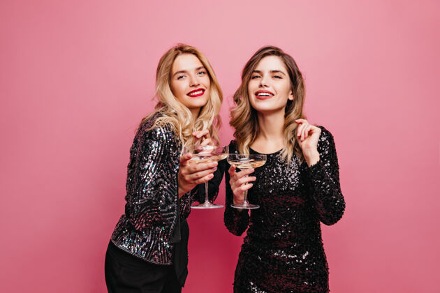 情感穿着得体的温文尔雅女孩在粉红色的墙上喝酒迷人的白种女人在聚会上放松微笑玩耍香槟