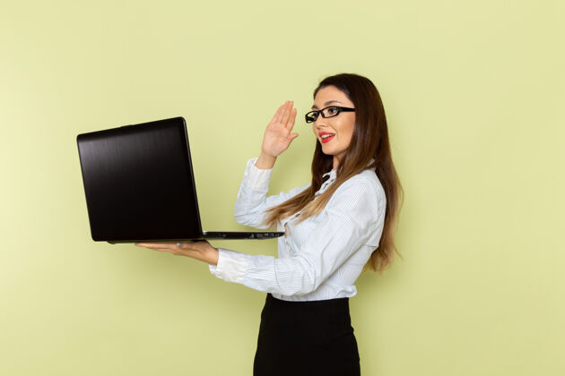 女士身穿白衬衫和黑裙子的女上班族在绿色墙上手持和使用笔记本电脑的正面图漂亮工人工作