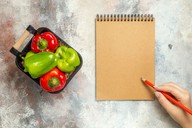 笔记本顶视图绿色和红色辣椒在碗里一个笔记本红色钢笔在女性手上裸体表面顶部碗甜椒