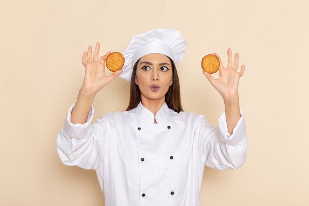 成人身穿白色厨师服的年轻女厨师正拿着饼干站在白墙上专业微笑肖像