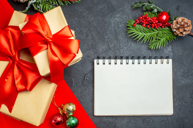 笔记本圣诞背景与蝴蝶结形彩带和笔记本杉木枝装饰配件在一个黑暗的表美丽的礼物冷杉蝴蝶结树枝