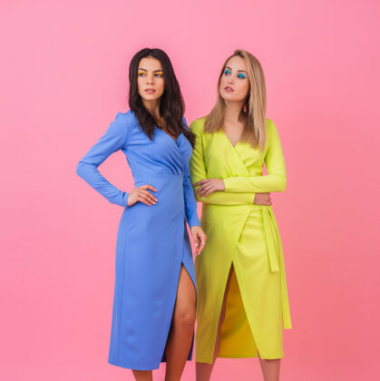 多彩两位时尚性感迷人的女士身着蓝黄相间的时尚多彩连衣裙 在粉色墙壁上摆出了一副丰满的姿势 夏日时尚潮流休闲色彩穿着