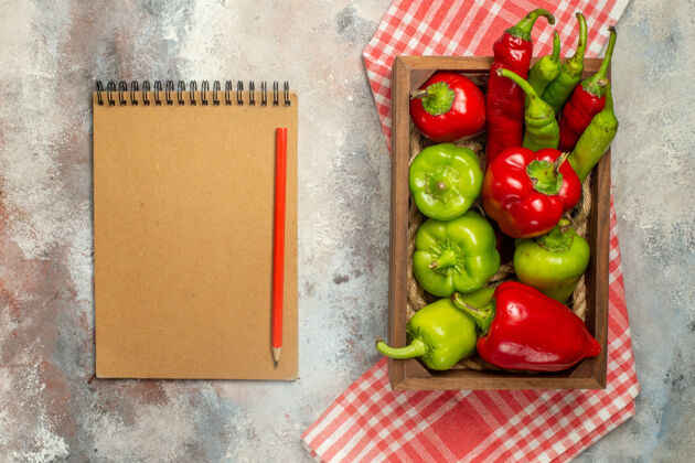 铅笔顶视图红色和绿色的辣椒辣椒在木箱中的格子桌布笔记本红色铅笔在裸体表面方格青椒和红椒顶部
