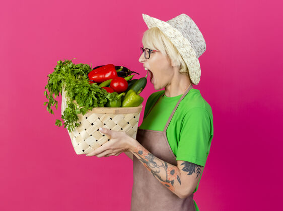 咬一位年轻的园丁 围着围裙 戴着帽子 手里拿着装满蔬菜的箱子蔬菜短裤年轻