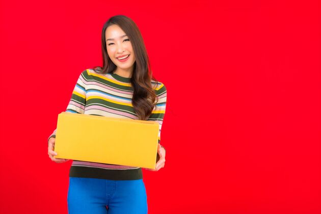 服务在红色的隔离墙上画一幅美丽的亚洲年轻女子拿着包裹盒微笑工作运输