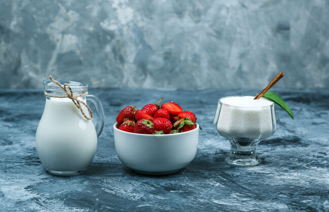 罐装平放一碗草莓在红色方格布毛巾上 一壶牛奶和一杯酸奶放在深蓝色大理石表面水平的自由空间为您的文字玻璃新鲜美味