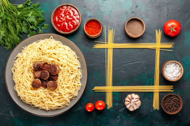生的顶视图煮熟的意大利面食 蓝色表面有肉丸和不同的调味品菜晚餐餐