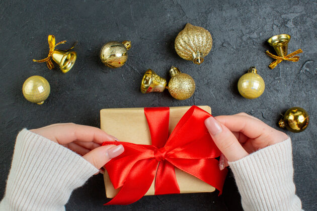 蝴蝶结手拿一个礼品盒的半张照片 红色丝带和深色背景上的装饰配件一半领结圣诞节