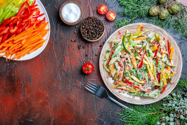 黑胡椒顶视图蔬菜沙拉在盘子叉子上盐和黑胡椒五颜六色的切辣椒西红柿在深红色的桌子上自由空间午餐切蔬菜