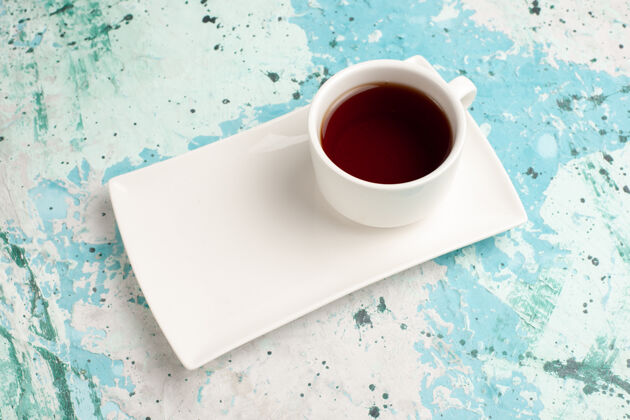 桌子浅蓝色桌子上的茶杯和盘子里有半杯茶热的饮料