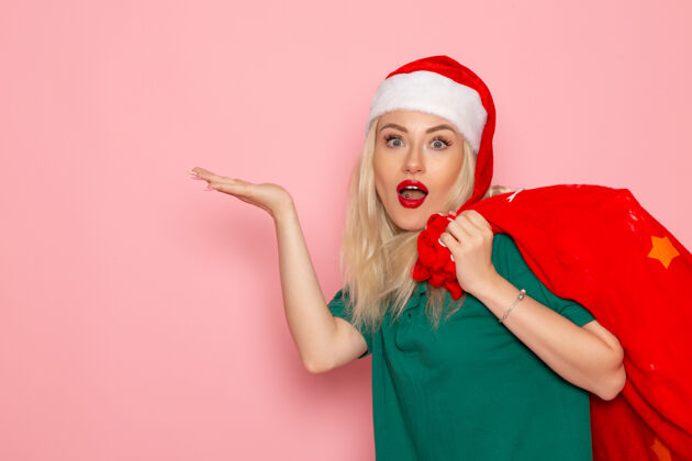 圣诞节正面图年轻女性提着红包带着礼物在粉色墙上度假模特圣诞新年彩照圣诞老人颜色风景年轻女性