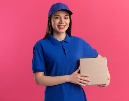微笑穿着制服的微笑漂亮的送货员拿着卡片盒隔离在粉红色的墙上 有复印空间女人抱着制服
