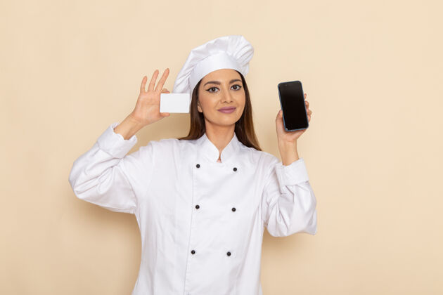 正面身穿白色厨师服的年轻女厨师的正面图 白色墙上拿着白色卡片和电话女性专业电话