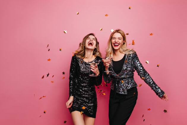 快乐欢笑的女士们在庆祝什么穿着闪亮连衣裙的女模特在粉红色的墙上跳舞女人情感成人