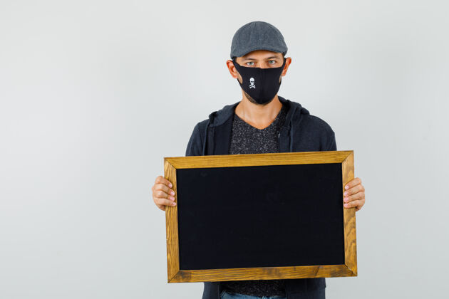 英俊身穿t恤 夹克 帽子 面具 正面照的手持黑板的年轻男性虚拟专业办公室