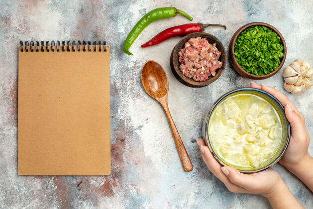 顶部俯瞰杜什巴拉饺子汤在一个碗里女人手大蒜辣椒木勺碗肉和绿色笔记本上裸体表面肉笔记本大蒜