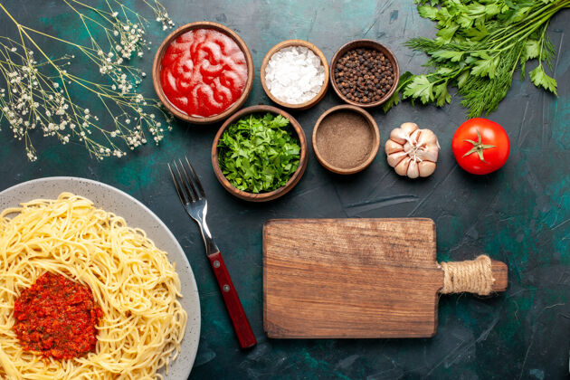 生的俯瞰煮熟的意大利面食 蓝色表面有肉和不同的调味品盘子宴会面食