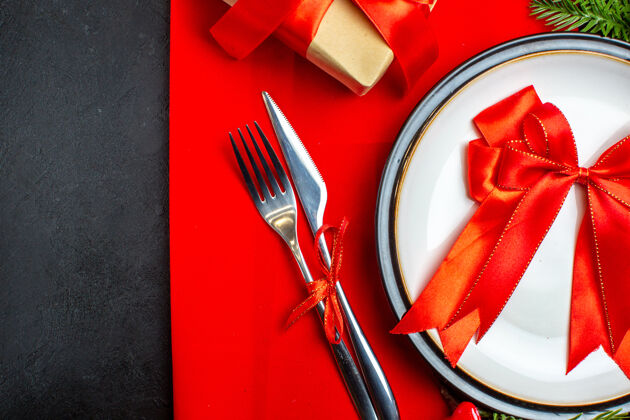 叉子新年背景上有红丝带的餐盘餐具套装装饰配件杉木树枝旁边有一个红色餐巾上的礼物抹刀餐盘胡椒