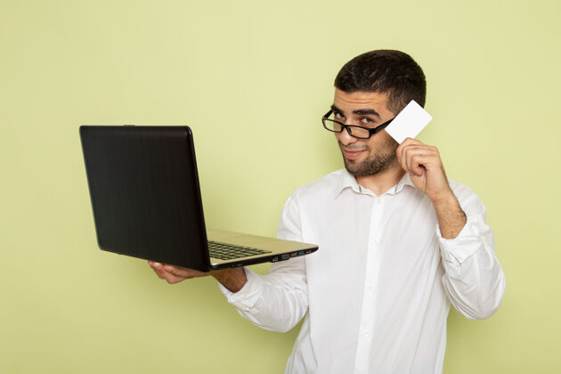人身穿白衬衫的男办公室工作人员手持并使用笔记本电脑在浅绿色墙上的正视图办公室持有工作