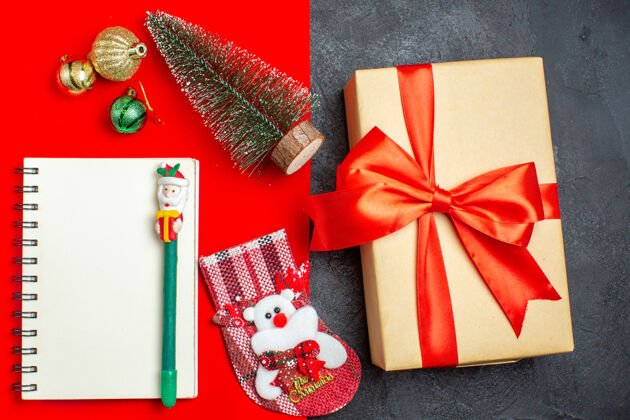 圣诞节顶视图美丽的礼物圣诞树袜子笔记本与笔上的红色和黑色背景上衣漂亮的礼物轮子