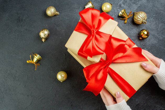礼品盒上图为手持一个带有红丝带的礼品盒和深色背景上的装饰配件风景轮子圣诞节