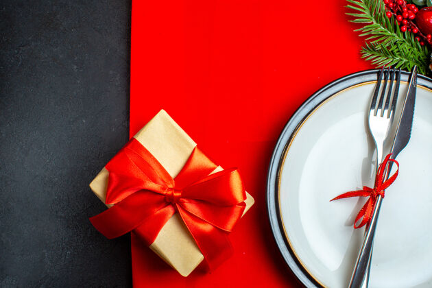 冷杉xsmas背景的半张照片 餐具套装 餐盘上有红丝带装饰配件杉木树枝 旁边是一张红色餐巾上的礼物圣诞节餐具餐巾