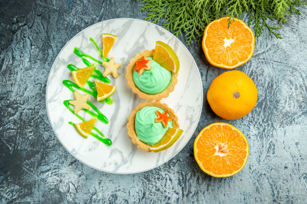 柠檬顶视图小馅饼与绿色糕点奶油和柠檬片在盘子上切橘子在黑暗的桌子上盘子柑橘新鲜