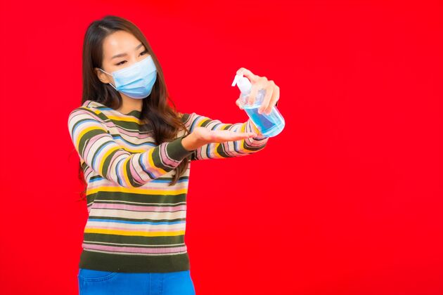 妇女用酒精凝胶在红色隔离墙上描绘美丽的亚洲年轻女子医药液体流感