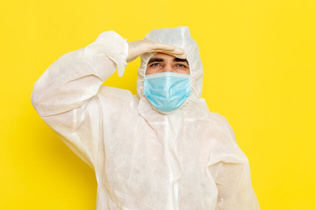 化学身穿白色特殊防护服 戴着无菌口罩的男性科学工作者正对着黄色墙上的远处看工人科学特殊