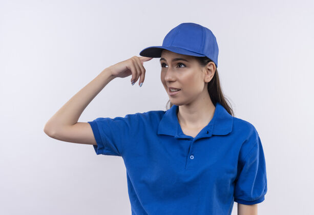 指向穿着蓝色制服 戴着帽子的年轻女送货员看起来很困惑 指着她的太阳穴说错话帽子错误女孩