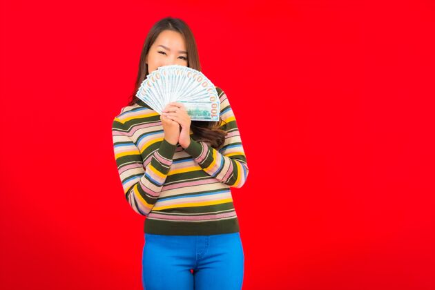 财富在红墙上画一幅美丽的亚洲年轻女子的画像 她手里拿着现金和手机货币在线微笑