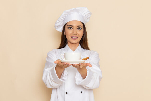 女身穿白色厨师服的年轻女厨师在浅白的墙上拿着咖啡的正面视图肖像手持厨房