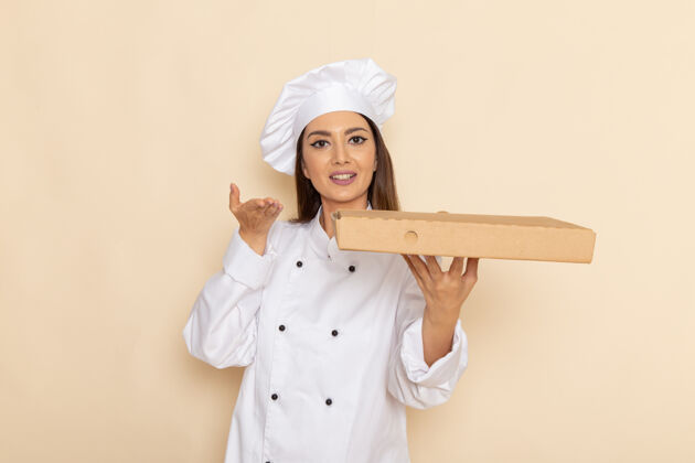 人身穿白色厨师服的年轻女厨师正拿着食物递送箱站在浅白的墙上女性工作烹饪