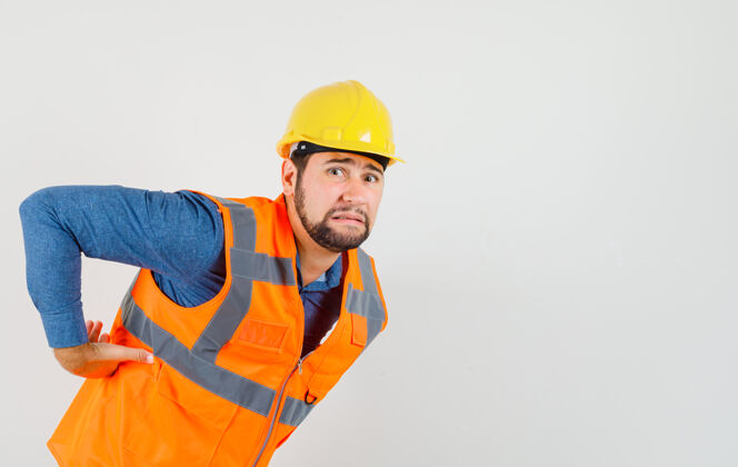 职业年轻的建设者在衬衫 背心 头盔和疲劳 前视图背痛建筑男杂工