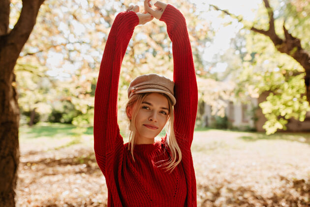 季节美丽的金发女孩在秋天的公园里感到快乐可爱的穿着红毛衣的女人在树叶间摆姿势公园颜色微笑
