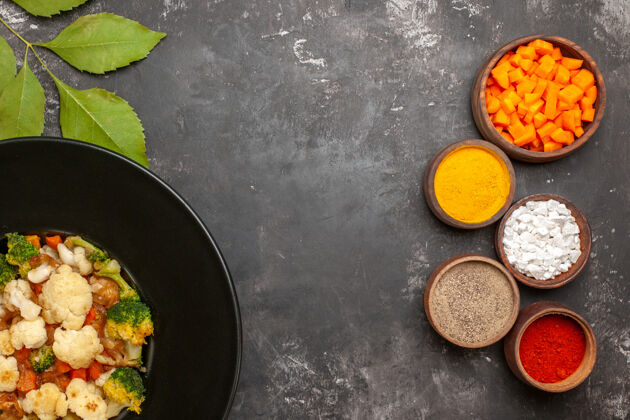 炊具顶视图西兰花和花椰菜沙拉在黑碗不同的香料和削减胡萝卜碗在黑暗的表面与复制sapce花椰菜和花椰菜切割平底锅