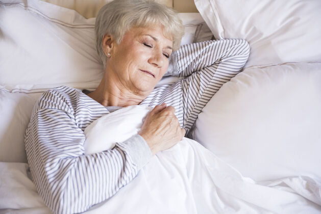 舒适睡在床上的疲倦的老妇人手放在头后面躺下休息