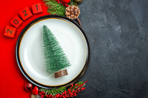 数字新年背景的水平视图与圣诞树晚餐盘装饰配件杉木树枝和数字在一个黑色的桌子上的红色餐巾容器盘子餐盘