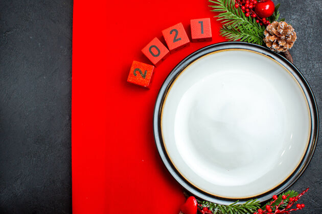 树枝新年背景用餐盘装饰配件杉木枝和数字放在一张红色餐巾上 黑色的桌子上横看餐巾碗冲压机