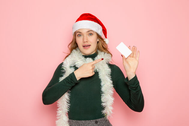 颜色正面图年轻女性手持白色银行卡在粉色墙面上的彩色情感模特过年肖像情绪圣诞