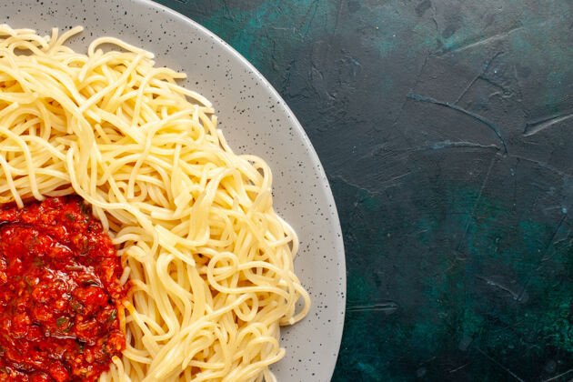 原料顶部近距离观看煮熟的意大利面食与肉末和番茄酱在深蓝色的表面意大利面肉晚餐