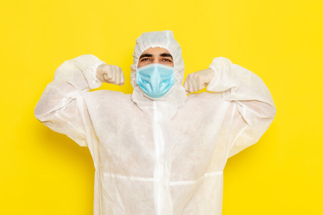 特殊身穿白色特殊防护服的男性科学工作者的正面图 黄色墙壁上的面具弯曲科学医疗男性