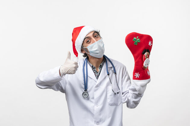 实验室外套正面图白色墙壁上戴着节日大袜子的男医生-圣诞节诊所冠状病毒圣诞节