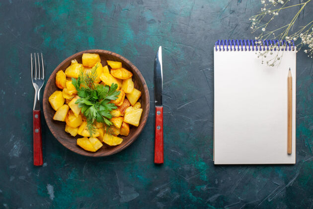 桌子俯瞰煮熟的土豆片 在深蓝色的桌子上放上带记事本的绿色美味套餐蔬菜午餐土豆