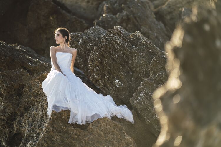 地平线选择性聚焦拍摄一位身穿白色连衣裙的黑发女性在岩石上摆姿势日落深色海洋