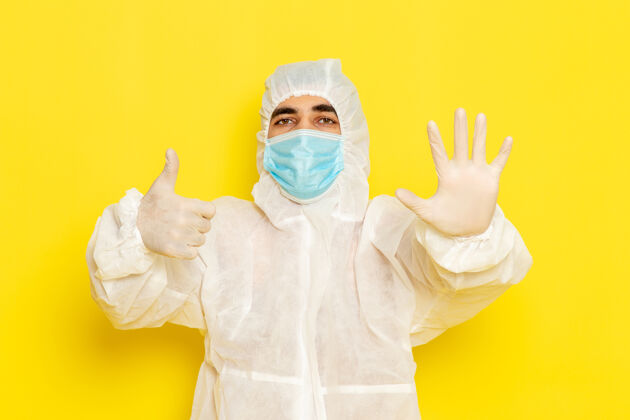 正面身穿特殊防护服 戴着面罩的男性科学工作者的正面图 手掌放在淡黄色的墙上男性服装危险