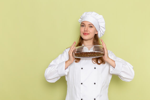 举行身着白色厨师服的女厨师正对着绿色墙壁上放着咖啡籽的罐子女帽子种子